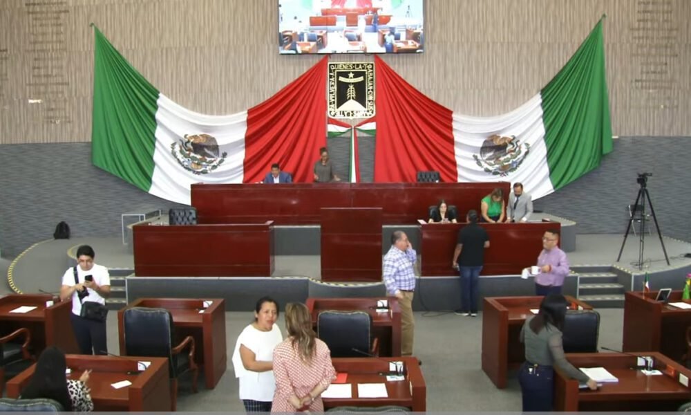 Sesión en Congreso de Morelos, varios diputados sentados y de fondo la bandera