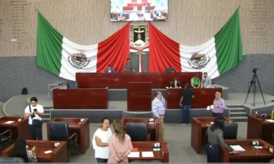 Sesión en Congreso de Morelos, varios diputados sentados y de fondo la bandera