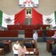 Sesión en Congreso de Morelos, varios diputados sentados y de fondo la bandera