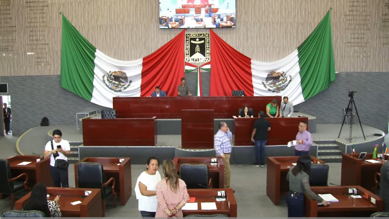 Sesión en Congreso de Morelos, varios diputados sentados y de fondo la bandera