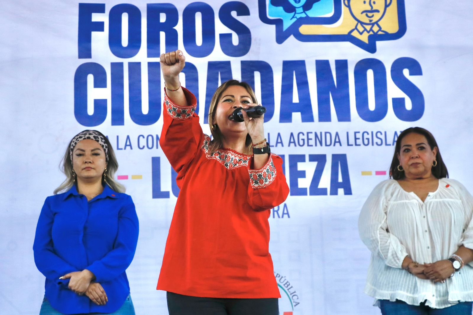 Senadora Lucy Meza de pie con la mano levantada en Foros Ciudadanos