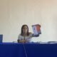 Mujer con una hoja en la mano sentada y al frente una mesa color morado
