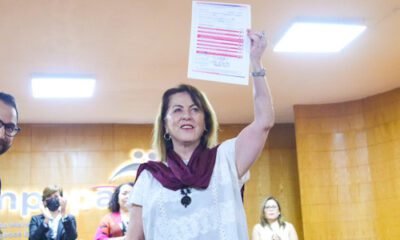 Margarita González con un documento en la mano, blusa blanca y mascada linda