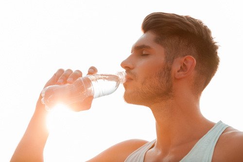 Joven con una botella de agua y sol de fondo