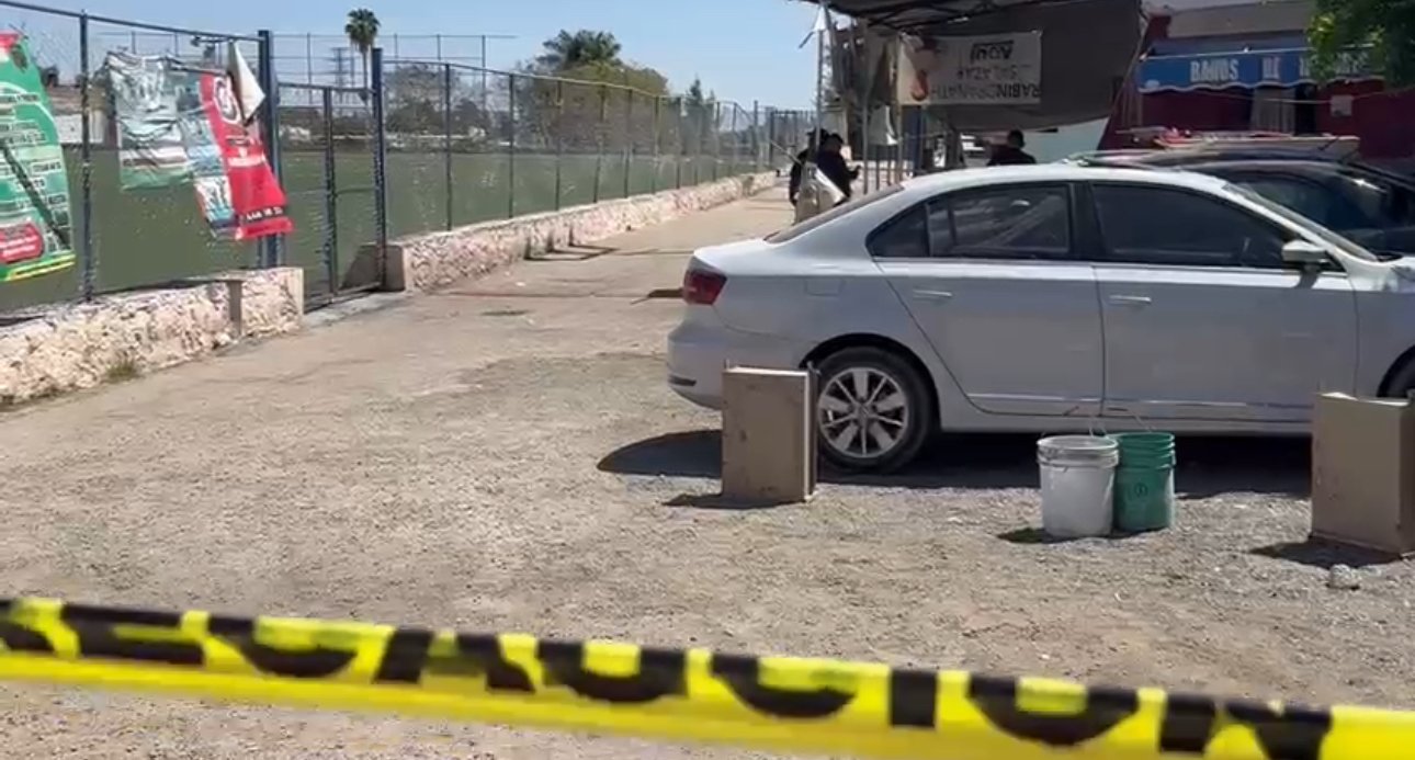 Cancha de fútbol, un auto blanco y una cinta acordonando la zona