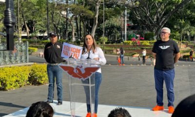 Mujer con tenis naranjas y blusa blanca, acompañada de dos hombres más con los logos de Movimiento Ciudadano