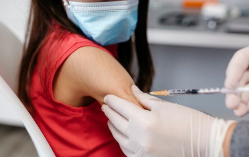 Una niña con blusa roja, descubierto el brazo y una jeringa