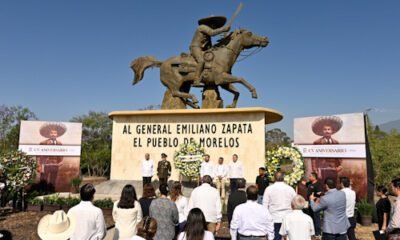 Estatua de Emiliano Zapata ofrenda floral y varias personas frente ala ofrenda