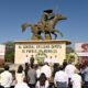 Estatua de Emiliano Zapata ofrenda floral y varias personas frente ala ofrenda